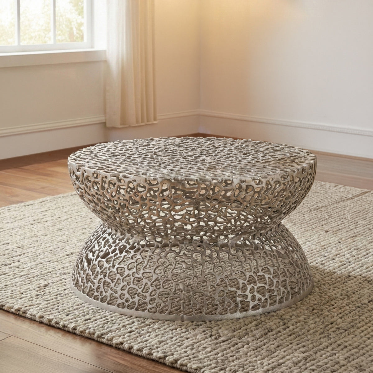 T3704 Silver round coffee table with an openwork pattern and hourglass-shaped base on a rug.