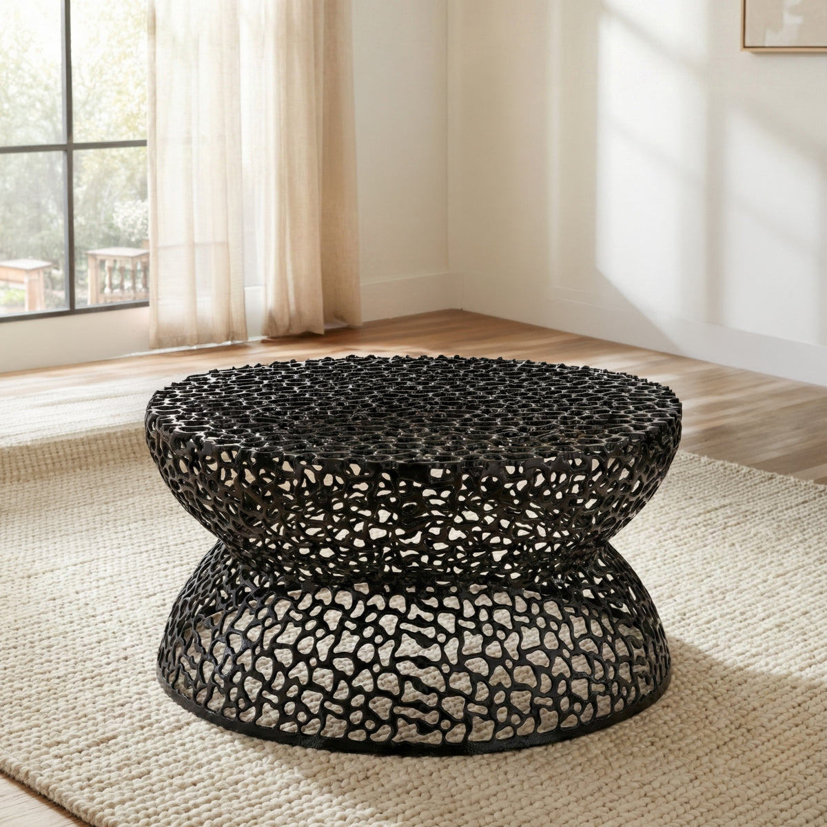 T3704 Black round coffee table with an openwork pattern and hourglass-shaped base on a rug.